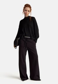 Schwarzer Strickpullover mit hohem Kragen und geripptem Saum, kombiniert mit lockeren schwarzen Hosen mit verstellbarem Kordelzug.