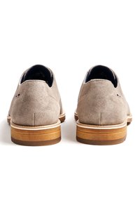 Chaussures en daim gris au design arrondi, avec une semelle en cuir marron et des accents de couleur claire autour de la semelle.