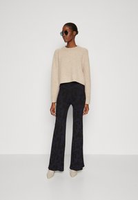 Pulover scurt bej, pantaloni cu model bleumarin și pantofi cu vârful ascuțit de culoare deschisă. Accesorizat cu ochelari de soare rotunzi.