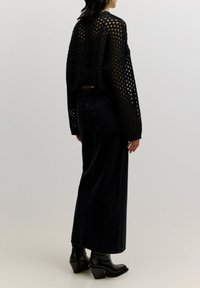 Zwarte opengehaakte trui met een cropped ontwerp, gecombineerd met hoge taille, donkere spijkerbroek en zwarte enkellaarsjes met hak.