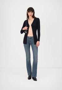Navy knit cardigan with deep V-neck, open front, and long sleeves; paired with light blue flared jeans and black ankle boots.