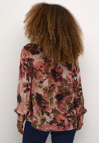 Blomsterbluse med et lyserødt og grønt mønster, lange ærmer med pyntede manchetter og guldbuttondetaljer. Letvægts, gennemsigtig stof.