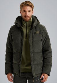 Chaqueta acolchada de color verde oscuro con un acabado texturizado, que presenta una capucha, cierre de cremallera y un parche con el logo en el pecho. Usada sobre una camiseta verde.