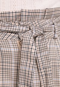 Brun rutigt tyg med en texturerad yta, som har ett knytbälte och en strukturerad midjeband. Blå och svarta accenter är utspridda i mönstret.