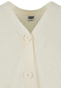 Cardigan couleur crème avec un décolleté en V, texture côtelée et trois boutons à l'avant. L'étiquette visible à l'intérieur indique "Urban Classics".