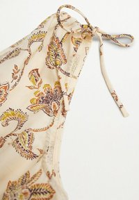 Tissu beige avec imprimé floral cachemire orange, jaune et marron, avec un cordon noué et bouclé dans un coin.