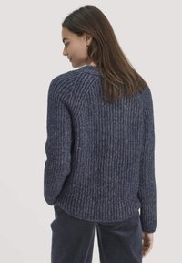Dunkelblaues, geripptes Strickpullover mit abgerundetem Saum und Raglanärmeln, der eine strukturierte Optik aufweist. Das Model hat lange Haare.