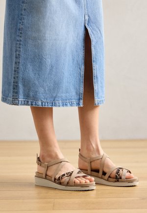 Beige sandaler med flere stropper, der har et leopardmønster som accent. Sålen er lysefarvet med en subtil tekstur, egnet til afslappet brug.