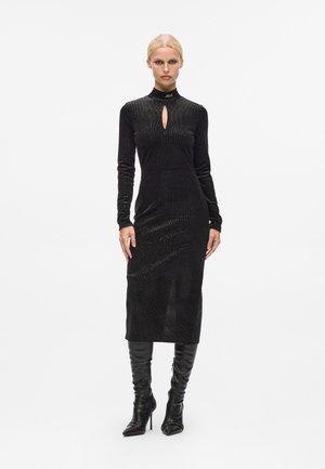 Black long-sleeve midi dress in soft, textured fabric with a keyhole neck detail. Model wears high-heeled, pointy-toed black boots.