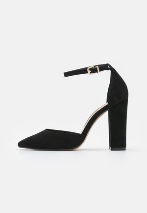 Zapatos de tacón alto de ante negro con punta puntiaguda, correa en el tobillo con hebilla dorada y diseño de tacón ancho y resistente.