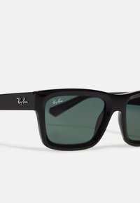 Ochelari de soare din plastic negru cu lentile verzi închise. Ramele pătrate au logo-ul Ray-Ban pe braț. Textură uniformă, fără modele vizibile.