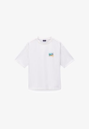 T-shirt en coton blanc à manches courtes, avec un patch graphique coloré brodé sur le côté gauche. Encolure ronde et coupe décontractée.