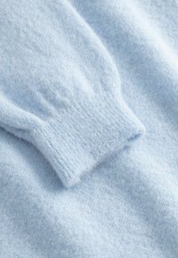 Svetlo modra mehka pletena tkanina s poudarkom na rebrastem manšetu na puloverju z dolgimi rokavi.