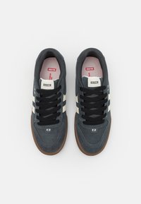 Para ciemnoszarych sneakersów Globe z czarnymi sznurowadłami, białymi paskami po bokach i brązowymi podeszwami, widziana z góry na białym tle.