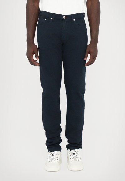 Donkerblauwe fitted jeans met een slim fit, vijf zakken ontwerp en metalen knoopsluiting, gecombineerd met witte sneakers.