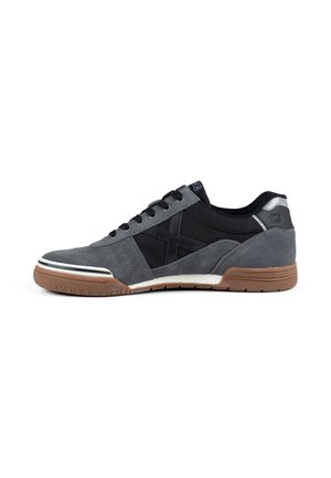 Zapatilla casual de corte bajo con parte superior de tela negra y gris y ante, suela de goma marrón, cordones negros y detalles cosidos en los paneles laterales.