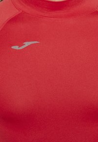 Rotes Sporthemd mit glatter Textur, kurzen Ärmeln und hohem Kragen. Enthält ein kleines silbernes Logo auf der linken Brust.