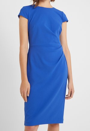 Femme portant une robe ajustée bleu roi longueur genou avec des manches courtes et un col rond haut sur un fond uni.