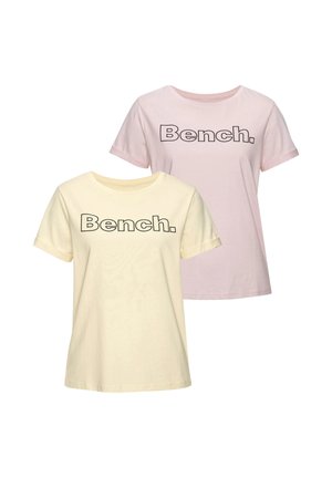 Zwei T-Shirts mit kurzen Ärmeln und Rundhalsausschnitt, eines hellgelb und eines hellrosa, jeweils mit dem Schriftzug „Bench.“ in fetten schwarzen Buchstaben.
