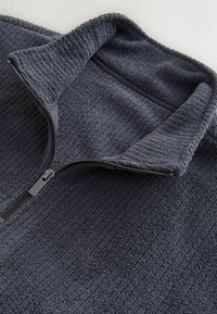 Dark gray fleece pullover with a high collar and half-zip closure. Textured fabric with ribbed lines and a flat zipper pull accent.