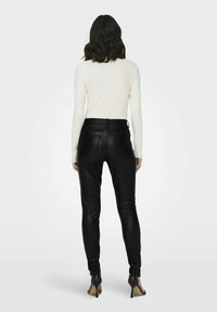 Pantalones de imitación de cuero negro con un ajuste ceñido, con bolsillos traseros y una cintura de altura media, combinados con una camiseta ajustada de manga larga blanca.