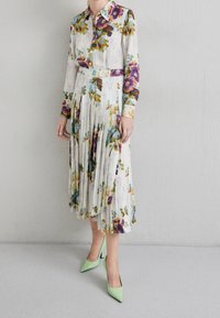 Květinové šaty s dlouhým rukávem a skladanou sukní, s živými fialovými a zelenými vzory na světlém pozadí. Doplněné mentolovými podpatky.