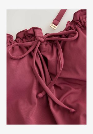 Bordowa tkanina z sznurkiem ściągającym i falbaniastym brzegiem; zawiera złote akcesoria oraz gładki, lekko teksturowany materiał.