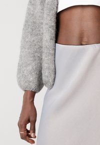 Cardigan tricotat de culoare gri deschis, cu mâneci bufante, asortat cu o fustă netedă de culoare argintie, cu o margine neagră la talie.