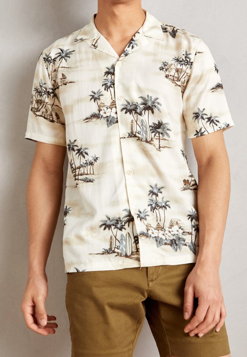 Korte mouwen shirt van lichtbeige stof met een tropische print van palmbomen, surfplanken en hutten. Knopsluiting aan de voorkant en een ontspannen pasvorm.