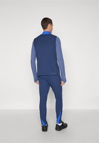 Navy blue athletic outfit featuring ribbed texture; long sleeves in two shades of blue; fitted design; contrasting blue accents on the pants.