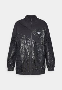 Black jacket with contrasting matte and shiny snake-print patterns, zip closure, high collar, and elastic cuffs. Reebok logo on upper left.