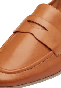 Mocassino in pelle marrone chiaro dal design elegante, con un dettaglio a punta, texture liscia e una suola di colore chiaro a contrasto.