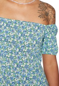 Vestido azul estampado com flores e mangas bufantes à off-shoulder, apresentando tons de azul e verde sobre um fundo claro, destacando padrões detalhados de flores.