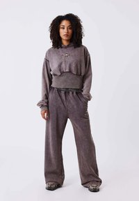 Sudadera gris de gran tamaño y corta, con cordón y logotipo, combinada con pantalones de chándal de pierna ancha en un tono similar, que cuentan con bolsillos y una textura suave.