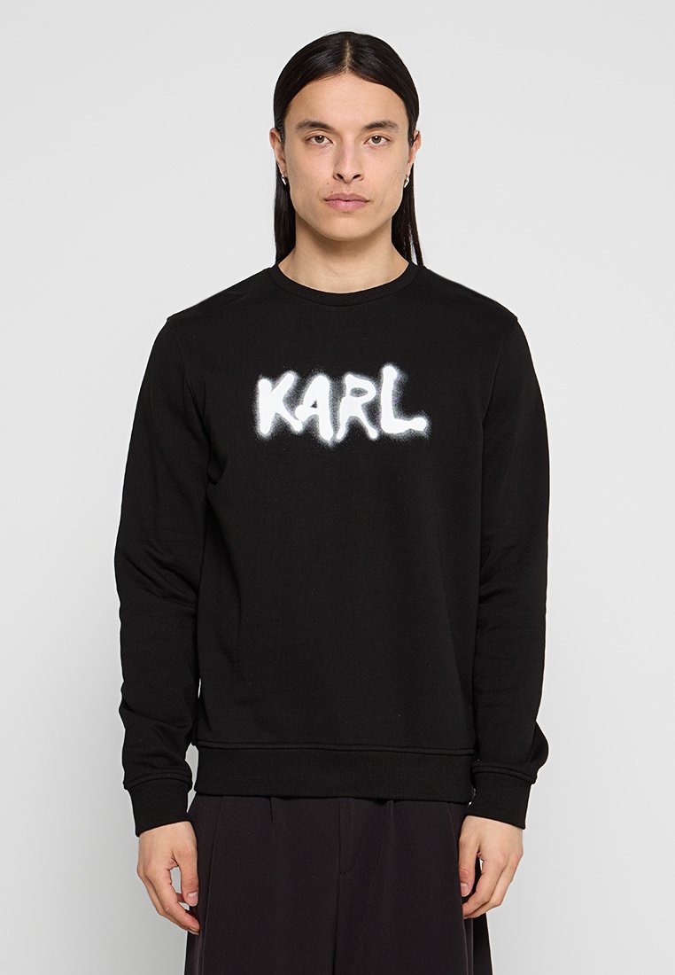 Sudadera negra de tela suave con un destacado logo en spray blanco "KARL" en el frente. Cuello redondo clásico y puños acanalados.
