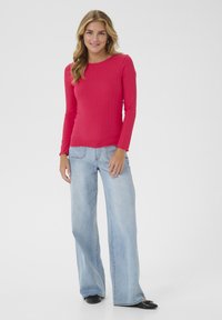 Long-sleeve ribbed top in bright pink, paired with light blue wide-leg jeans. Features a round neckline and frilled sleeve edges.