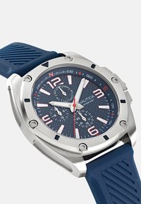 Reloj Nautica con caja de acero inoxidable, correa de caucho azul, esfera texturizada de color marino, marcadores de horas en blanco y rojo llamativos, y subesferas de cronógrafo.