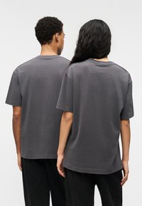 Γκρι κοντομάνικα T-shirts με χαλαρή εφαρμογή, κατασκευασμένα από απαλό βαμβάκι, με στρογγυλή λαιμόκοψη και ίσια τελειώματα, φορεμένα από δύο άτομα από πίσω.