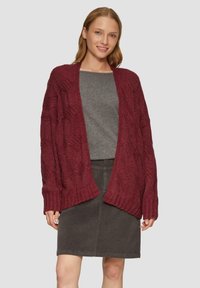 Burgunderfarbener Strickcardigan mit offener Vorderseite, strukturierten Mustern und gerippten Manschetten, kombiniert mit einem grauen Oberteil und einem dunkelgrauen Rock.