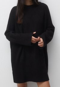 Robe pull oversized noire en maille douce, avec un col rond et des manches longues à larges poignets.