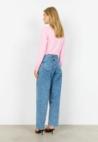 Pikad varrukad roosa pluus, kinnitatud kõrge vöökohaga, lahtise istuvusega hele sinine teksapüks. Omab sirget sääreosa ja peeneid kulumise detaile.