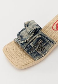 Δερμάτινα πέδιλα από τζιν με υφασμένη υφή από φυτική ίνα, με διακοσμητική τσέπη και λεπτομέρεια φερμουάρ στη λωρίδα, σε μπλε και μπεζ χρώματα.