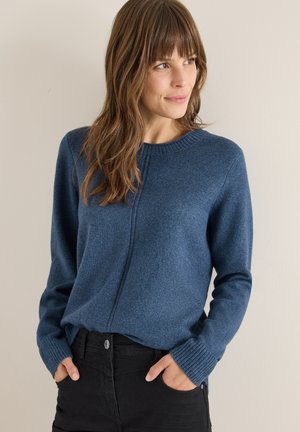 Blauer Strickpullover mit rundem Ausschnitt, gerippten Bündchen und geradem Schnitt. Über schwarzen Jeans getragen, zeigt eine glatte Textur.