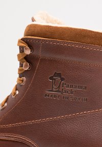 Botas de cuero marrón con forro de pelo sintético, sistema de cordones único y logotipo grabado. Costuras duraderas y elementos de diseño elegantes.