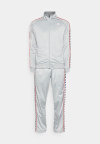 Survêtement Kappa gris clair avec veste zippée et pantalon assorti, avec un liseré rouge et des bandes de logo répétées sur les manches et les jambes.