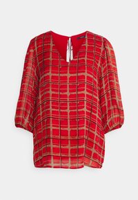 Blusa roja con estampado, con escote en V, silueta holgada, mangas de tres cuartos y un detalle de lazo en la parte posterior. Presenta un diseño a cuadros en color dorado.