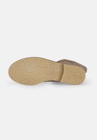Zapato de ante marrón con una suela de goma texturizada en color marrón claro. La suela presenta un patrón ondulado y cuenta con un logotipo de la marca grabado. No tiene embellishments visibles.