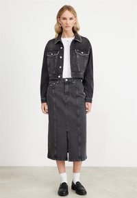Fekete farmer cropped dzseki gombos elülső résszel, két mellzsebből és kontrasztos fehér varrással; magas derekú fekete farmer szoknyával párosítva.