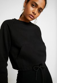 Black cropped sweatshirt with a round neckline, elastic waist, and a front pocket. Smooth texture and raglan sleeves.