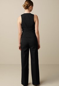 Czarny bezrękawnik z dopasowanym topem i prostymi spodniami, o gładkiej fakturze i czystych liniach, widziany od tyłu.